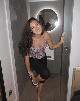 Coralie smiling in a doorway, holding one foot up