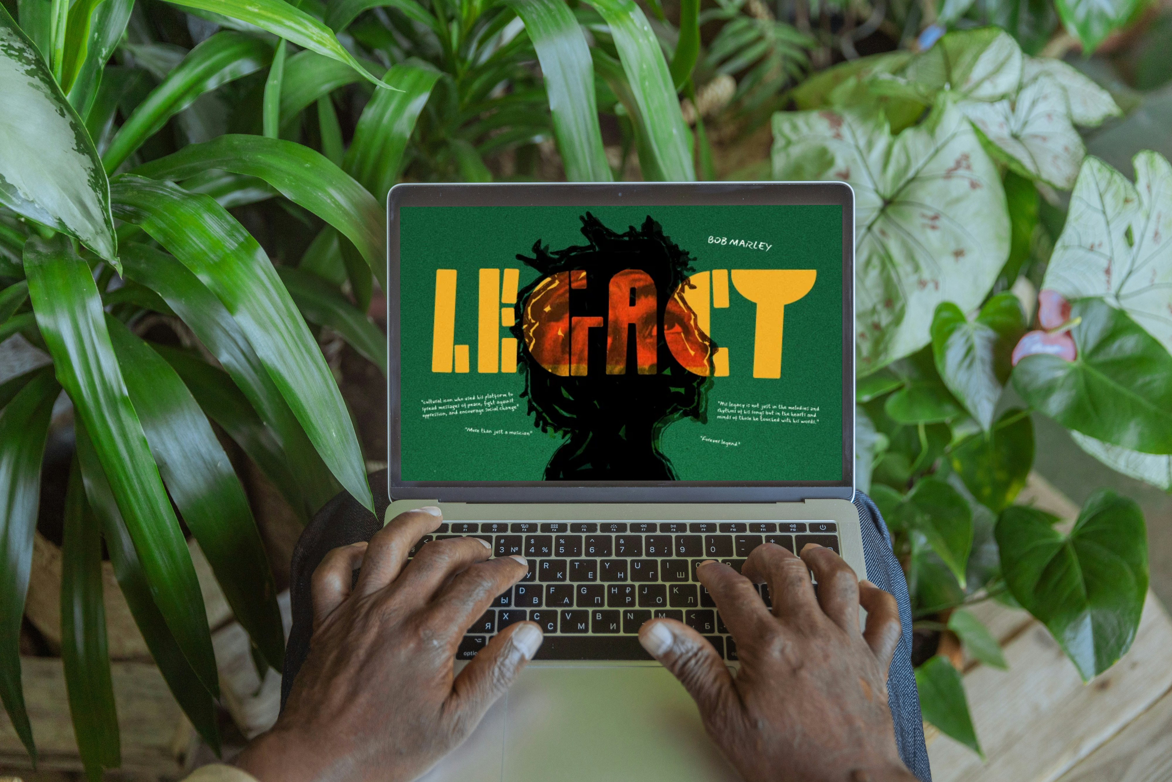 Hands typing on a laptop among plants, the screen showing the Legacy page